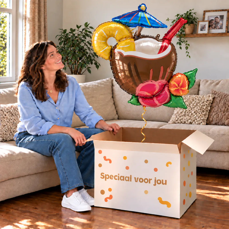 Een vrouw kijkt blij naar Kokosnoot Cocktail Pina Colada XL boven een grote Speciaal voor jou-doos in een warme woonkamer.