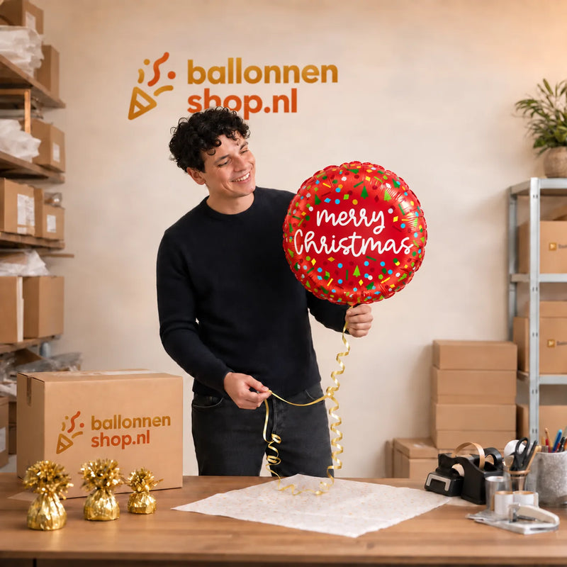 Jesse houdt de Merry Christmas Confetti Ballon vast in de warme werkplaats van Ballonnenshop.nl.