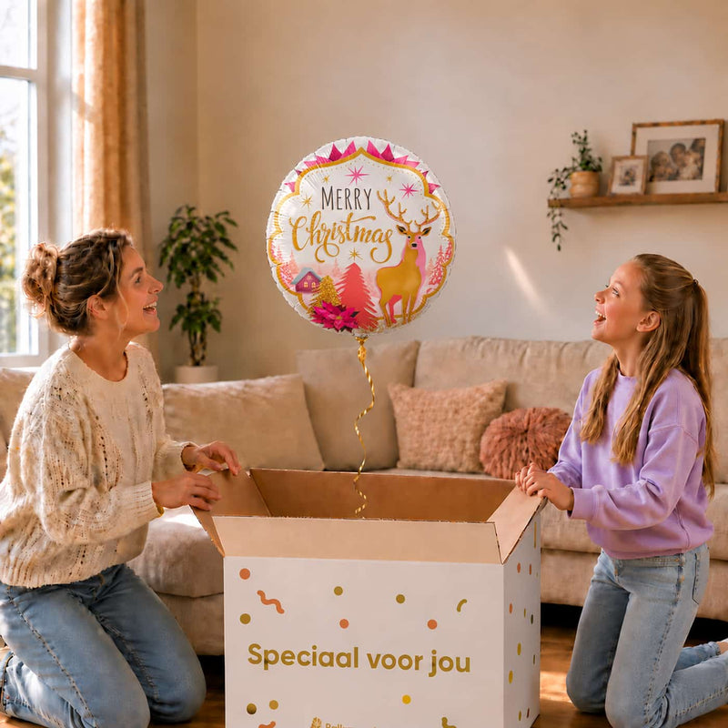 Moeder en meisje openen een cadeaudoos met een Merry Christmas ballon van 46 cm met een hert en roze kerstversiering.