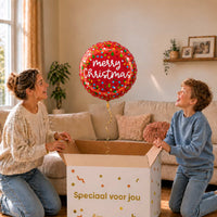 Moeder en jongetje pakken een rode Merry Christmas confettiballon van 46 cm uit een cadeaudoos.