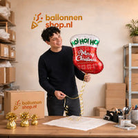 Jesse houdt de Merry Christmas Sok Helium Ballon vast in de warme werkplaats van Ballonnenshop.nl.