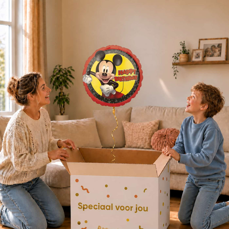 Moeder en jongen bekijken de ballon Mickey Mouse Happy Birthday in zacht warm licht boven de geopende cadeaudoos ‘Speciaal voor jou’.