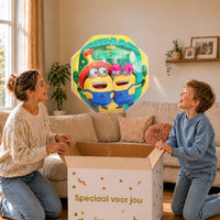 Moeder en jongen bekijken een Minion Embrace Your Friends-ballon van 65 cm met gouden lint boven de geopende cadeaudoos ‘Speciaal voor jou’.