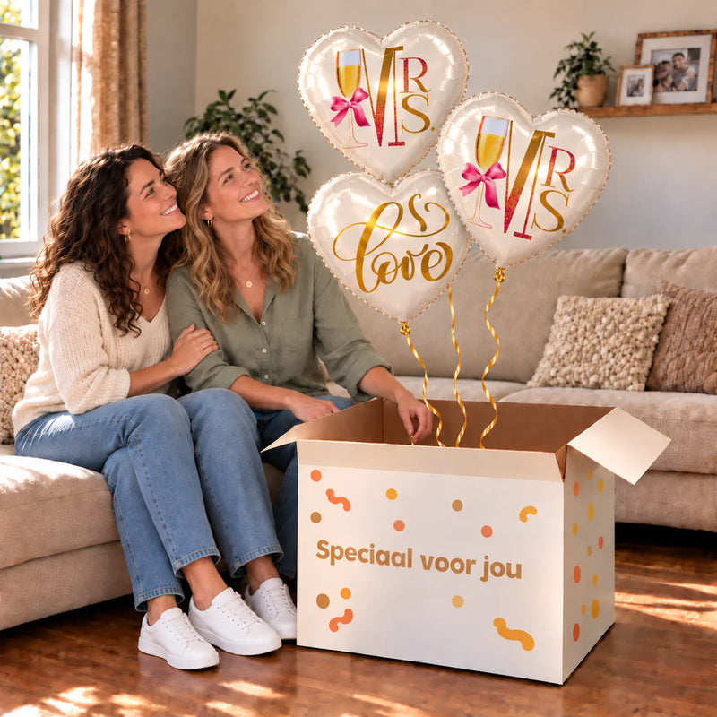 Een feestelijk huwelijksmoment met Mrs & Mrs Love Trosje Ballonnen boven een open Speciaal voor jou-doos in een warme woonkamer.