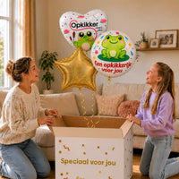 Opkikker Voor Jou Trosje: moeder en dochter pakken twee kikkerballonnen en een gouden ster uit een cadeaudoos, met drie krullinten die samenkomen in de doos.