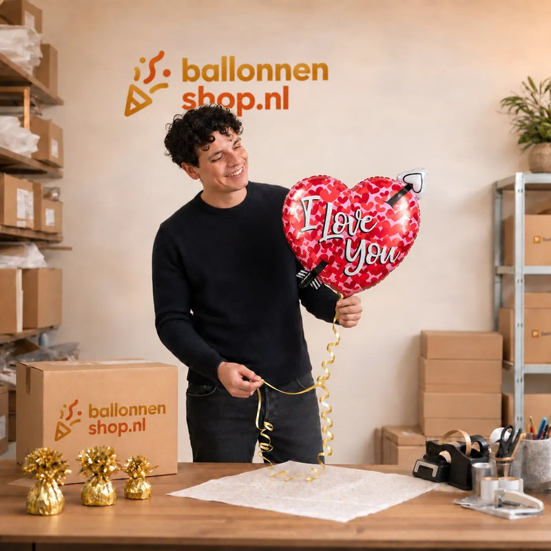 Jesse houdt de Pijl Door Hart I Love You Hart Ballon vast in de warme werkplaats van Ballonnenshop.nl.