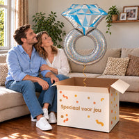 Een volwassen stel kijkt blij naar Platinum Zilveren Ring XL Ballon boven een grote Speciaal voor jou-doos in een warme woonkamer.