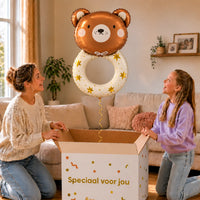 Rammelaar Beer Helium XL Ballon zweeft boven een geopende cadeaudoos bij een moeder en meisje in een warme woonkamer.