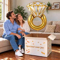 Een volwassen stel kijkt blij naar Ring Helium XL Ballon boven een grote Speciaal voor jou-doos in een warme woonkamer.