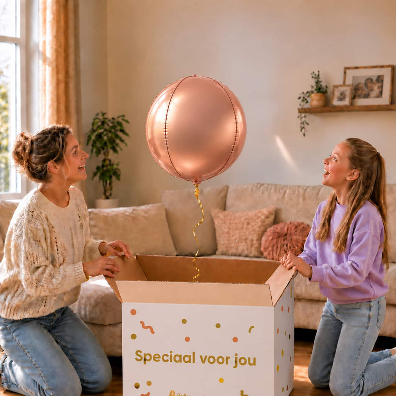 Moeder en meisje bekijken een roségouden ronde bolballon van 45 cm boven de cadeaudoos.