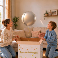 Moeder en jongen bekijken een zilveren ronde bolballon van 45 cm boven de cadeaudoos.