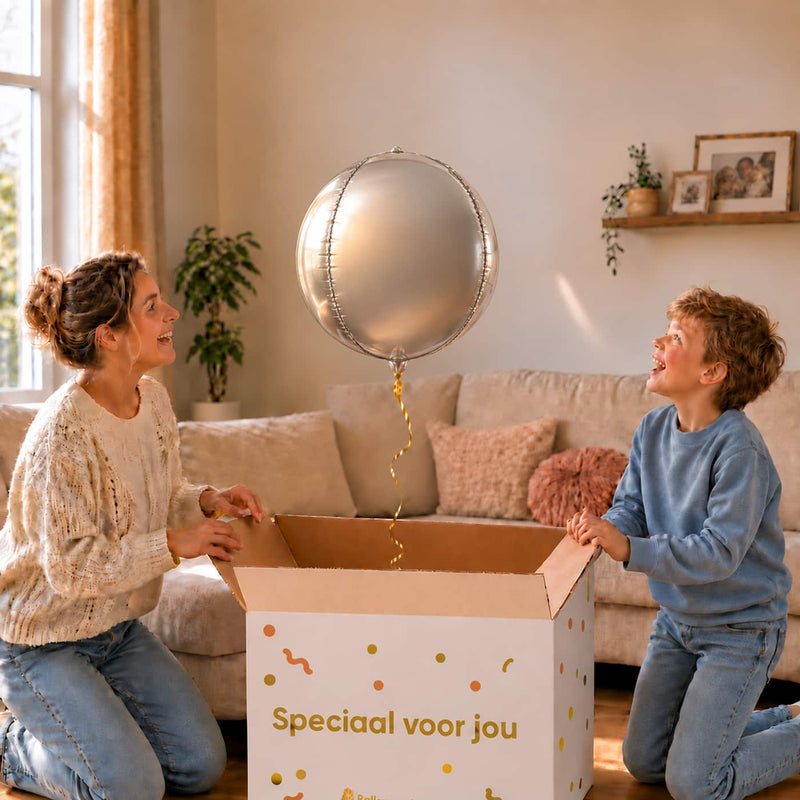 Moeder en jongen bekijken een zilveren ronde bolballon van 45 cm boven de cadeaudoos.