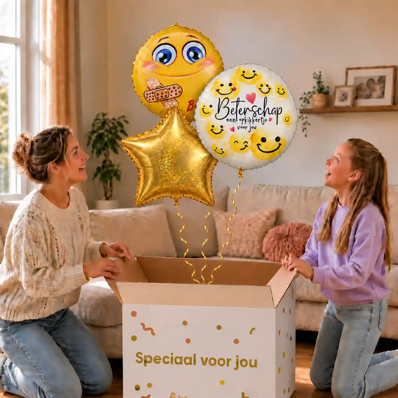 Smiley Beterschap Trosje: moeder en dochter pakken twee smileyballonnen en een gouden ster uit, met drie gouden krullinten die samenkomen in de cadeaudoos.