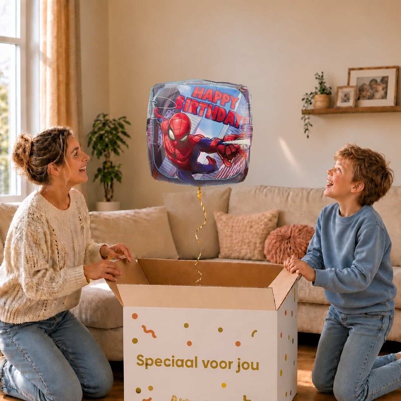 Moeder en jongen bekijken een Spiderman Happy Birthday-ballon boven de geopende cadeaudoos ‘Speciaal voor jou’ in zacht warm licht.