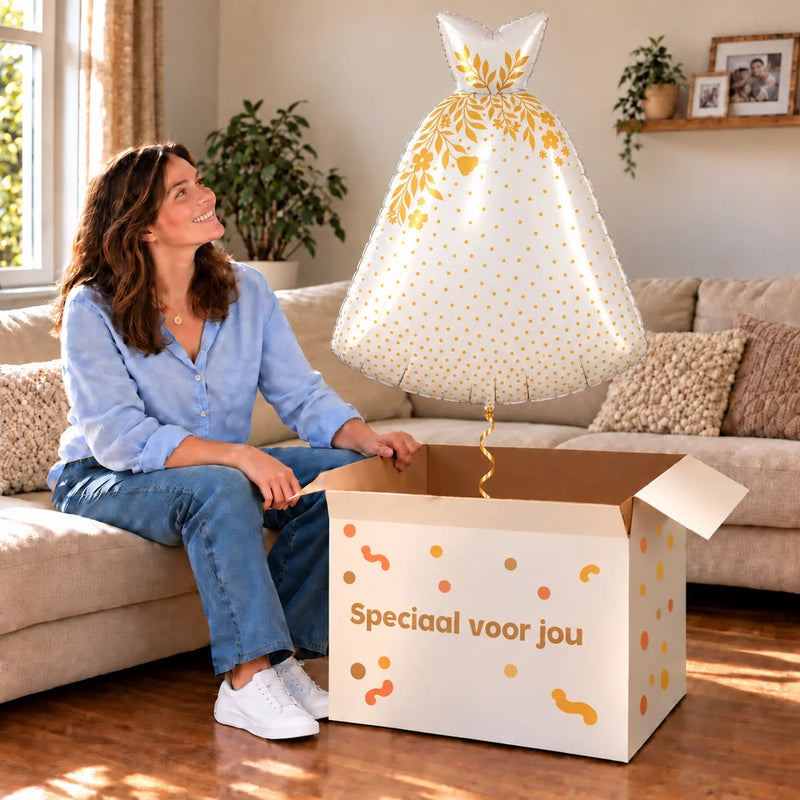 Een vrouw kijkt blij naar Trouwjurk Helium XL Ballon boven een grote Speciaal voor jou-doos in een warme woonkamer.