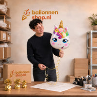 Een medewerker houdt de Unicorn Helium Ballon met gouden hoorn en regenboogmanen vast bij de inpaktafel.