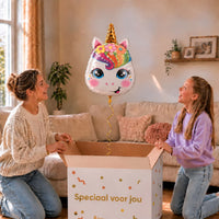 Moeder en meisje bekijken een eenhoornballon met gouden hoorn en regenboogmanen boven de geopende cadeaudoos ‘Speciaal voor jou’.