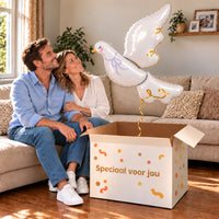 Een volwassen stel kijkt blij naar Witte Duif Helium XL Ballon boven een grote Speciaal voor jou-doos in een warme woonkamer.