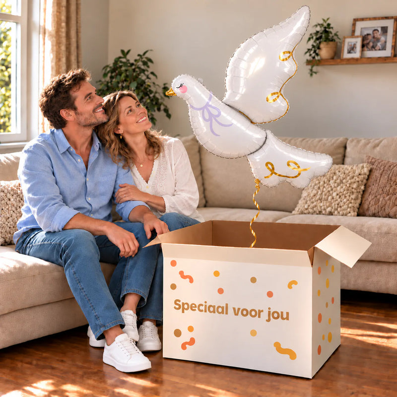 Een volwassen stel kijkt blij naar Witte Duif Helium XL Ballon boven een grote Speciaal voor jou-doos in een warme woonkamer.