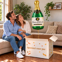 Een volwassen stel kijkt blij naar Champagne Fles Helium XL Ballon boven een grote Speciaal voor jou-doos in een warme woonkamer.