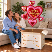 Een volwassen stel kijkt blij naar XL Happy Valentine’s Day – Voor een Bijzonder Moment boven een grote Speciaal voor jou-doos in een warme woonkamer.