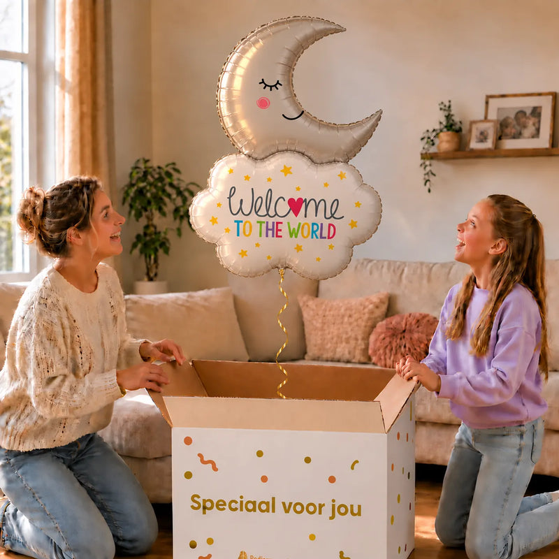 Welcome To The World Maan XL zweeft boven een geopende cadeaudoos bij een moeder en meisje in een warme woonkamer.